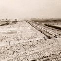 Nwe Statenzijl -19  Deze foto is gemaakt vanaf de zeedijk aan de Duitse kant. De onverharde weg loopt langs de grens tussen Nederland en Duitsland. Aan de rechterkant van de weg ligt Nederland, rechts ligt Duitsland. Achteraan, links van het midden is een stuk nieuwe dijk aangelegd, met daarop een gemaal. In de verte zijn enkele boerderijen te zien van de Kroonpolder. (Foto: Harm Hillinga, 1969).